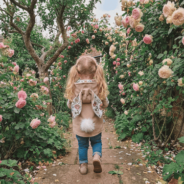 Child walking through a garden with pink roses wearing a gilet with bunny ears and white fluffy tail