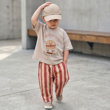 Toddler boy wearing red and orange striped trousers with a Suns out buns out printed t-shirt