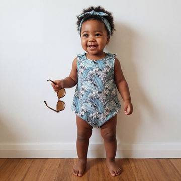 Toddler girl wearing tropicana leaf print summer baby and toddler romper with matching headband
