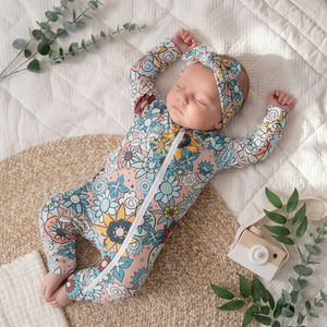 Sleeping baby girl wearing Lottie & Lysh Zipped sleepsuit with retro floral design, and matching headband.
