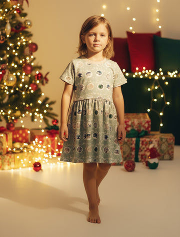 Young girl in a festive dress standing in front of a decorated Christmas tree and presents.