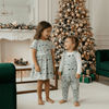 Two children in matching outfits standing in a festive living room with a decorated Christmas tree.