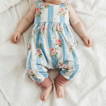 Baby wearing a floral and striped romper on a white blanket