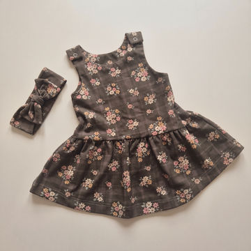 A toddler girl's sleeveless dress with a matching fabric headband, laid flat on a light beige background. The dress is dark gray with a small-scale floral print in pink, white, and yellow, and features a gathered waist.