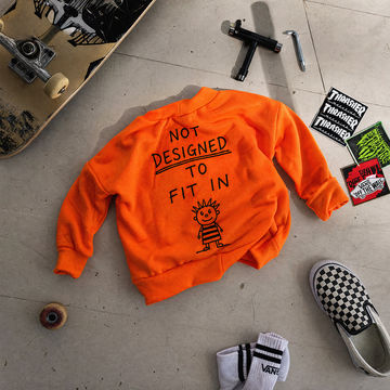Orange sweatshirt with text and graphics on a concrete floor with skateboards and shoes.