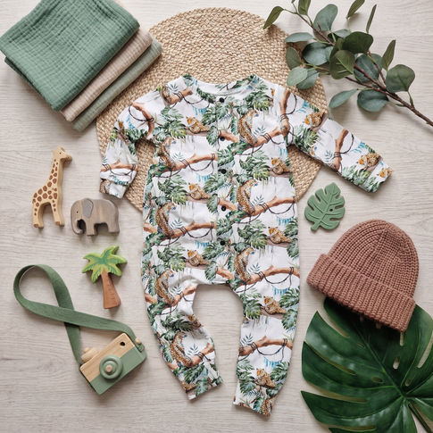 Baby romper with animal print surrounded by toys and a hat on a light wooden surface.