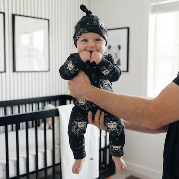 Baby in black outfit with mandala lion head held by an adult in a nursery.