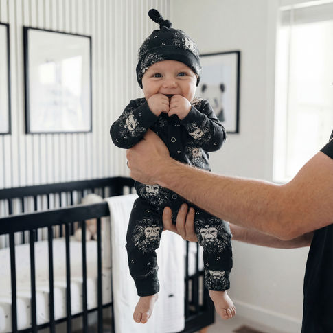 Baby in black outfit with mandala lion head held by an adult in a nursery.