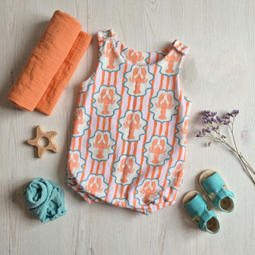 Baby outfit with patterned romper, orange swaddle, blue socks, and shoes on a light wooden surface.