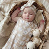 sleeping baby girl wearing a beige romper with white daisy detail with matching bow headband