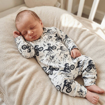 Newborn baby sleeping in a crib wearing a onesie with black patterns.