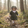 whimsical image of a little girl wearing an olive green coat with bunny ears, carrying a toy bunny, in a woodland scene.