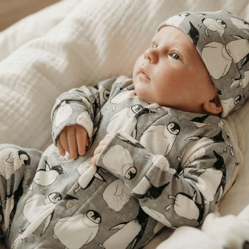 Baby wearing a gray outfit with penguin patterns on a soft surface