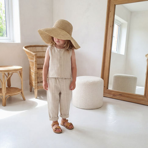 Child wearing a wide-brimmed hat in a minimalistic room with a mirror and wicker chair.