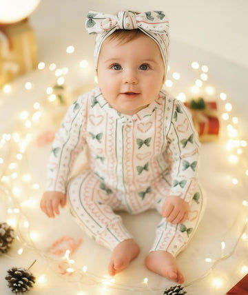 Baby wearing a christmas outfit and headband surrounded by string lights and pinecones.