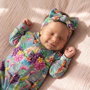 Smiling sleeping baby girl wearing Lottie & Lysh hummingbird babygrow and headband set. 