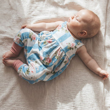 Baby lying on a textured blanket wearing a floral romper with blue stripes