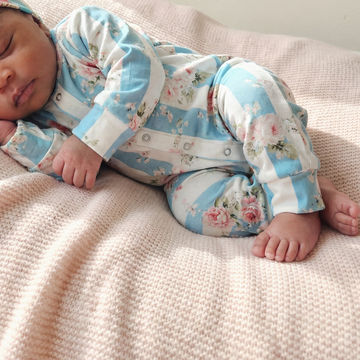 Newborn baby wearing a floral onesie on a soft pink blanket