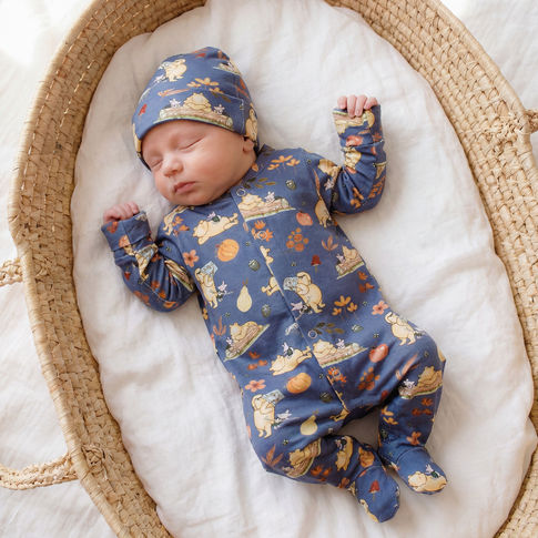 Newborn baby in a winnie the pooh patterned outfit and hat lying in a woven basket.