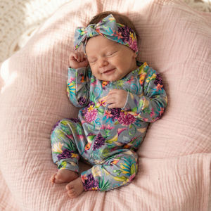 A smiling newborn baby girl wearing a hummingbird babygrow and matching baby headband
