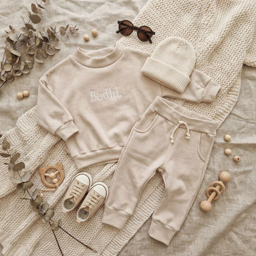 Beige baby outfit with 'Bodhi' on a textured surface with decorative elements.