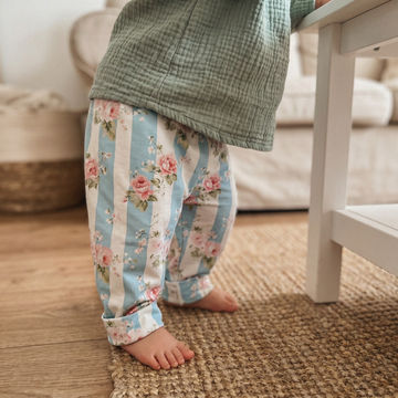 Child wearing floral striped pants and a green checkered shirt in a home setting.
