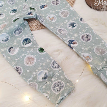 A close up photo of Lottie & Lysh's Christmas Bauble print leggings. The fabric is light green with garlands of christmas baubles showcasing different wintery scenes. 