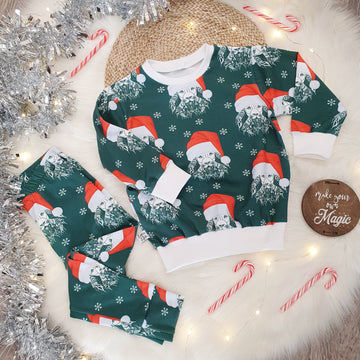 Children's christmas leggings. Green background featuring a special edition print of Lottie & lysh's signature Lion print wearing a red and white santa style hat. White snowflakes adorn the background. The leggings are photographed against a white fluffy background with silver tinsel, red and white candy canes and fairy lights.