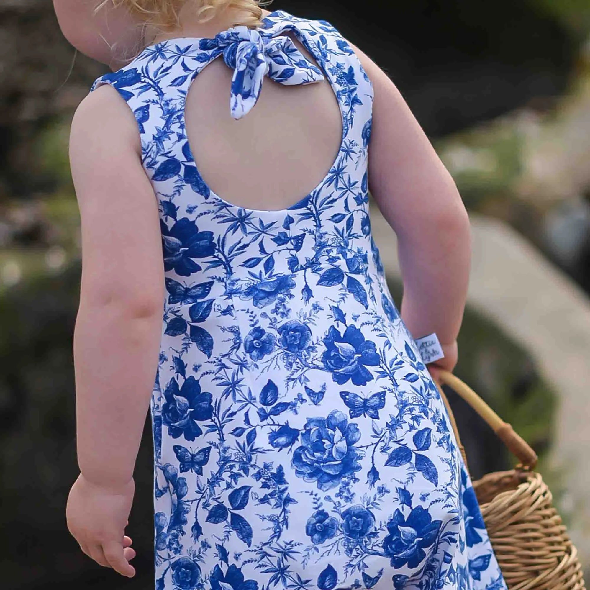 A photo showing the back of the Lottie & Lysh bow back romper. This little girl has blonde, curly hair and is wearing a blue and white floral playsuit.