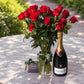 Long stem red roses in a glass vase beside a bottle of Bollinger Special Cuvée champagne