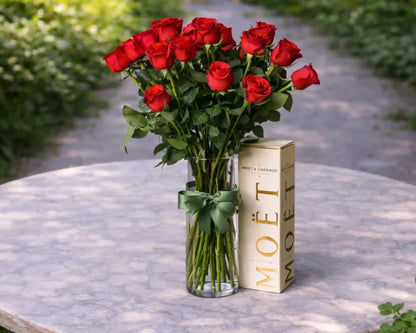 Long stem red roses in a glass vase beside a Moët champagne gift box