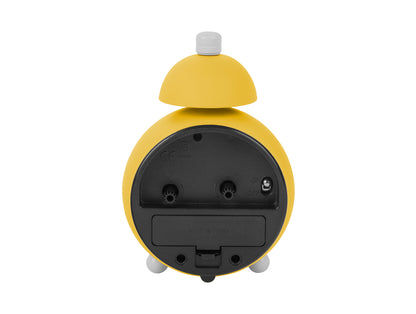 Ljusgul väckarklocka sedd bakifrån: batterifack och anslutningsöppningar synliga.