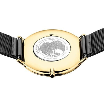 Fond de montre pour femme avec motif de carte du monde dans un boîtier doré et un bracelet en maille noire.