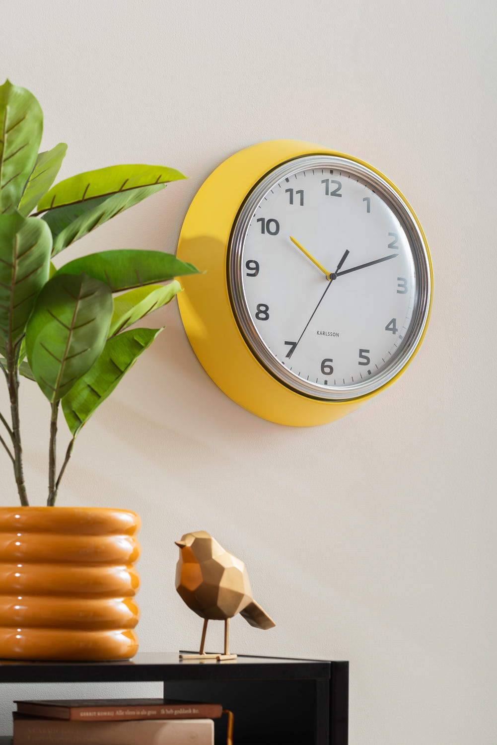 Horloge murale jaune avec cadran blanc et cadre noir, aiguilles visibles.