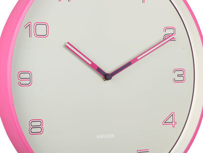 Närbild på väggklocka: beige urtavla med rosa siffror och visare