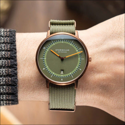 Montre unisexe avec cadran vert et bracelet textile couleur olive, finition cuivre.