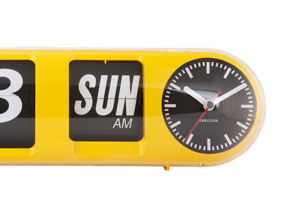 Gros plan sur une horloge murale jaune : chiffres à bascule avec SUN AM et heure analogique