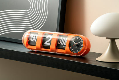 Horloge murale orange sur une étagère avec affichage à chiffres rabattables et cadran analogique
