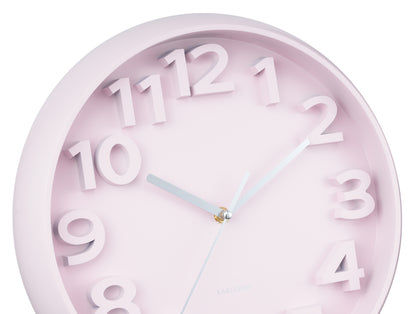 Détail de l'horloge murale : bordure rose pâle, grands chiffres arabes et aiguilles