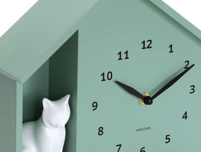 Détail de l'horloge murale : chat assis à gauche, aiguilles noires sur un cadran couleur menthe