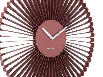 Väggklocka i närbild: röd urtavla med vita visare och lamellring