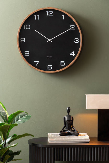Grande horloge murale Karlsson au mur : cadran noir avec bordure et aiguilles effet bois