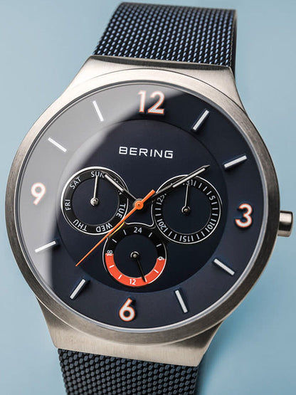 Bering Herrenuhr mit blauem Zifferblatt, orangefarbenen Akzenten und Milanaise-Armband