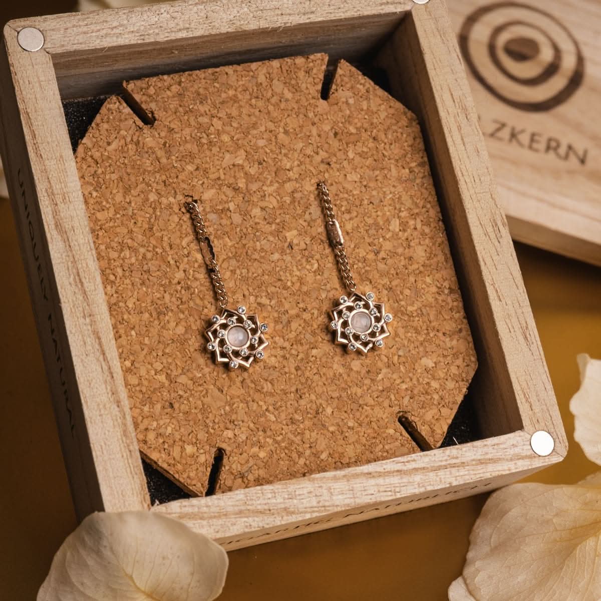 Boucles d'oreilles dans une boîte à bijoux : pierre ronde dans une couronne florale, chaîne avec crochet d'oreille
