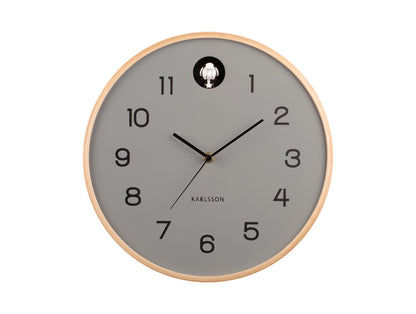 Horloge murale avec cadran gris, cadre en bois clair et figurine de coucou à 12h