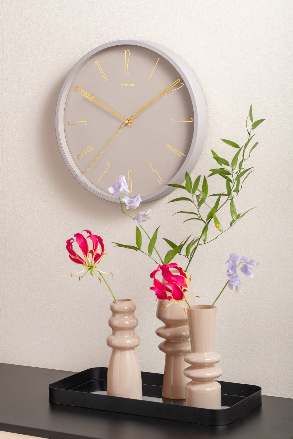 Horloge murale sur un mur avec un cadre gris chaud, un cadran beige et des aiguilles dorées