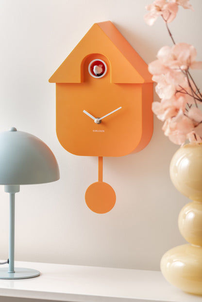 Orange väggklocka i husdesign med urverk och runt pendel
