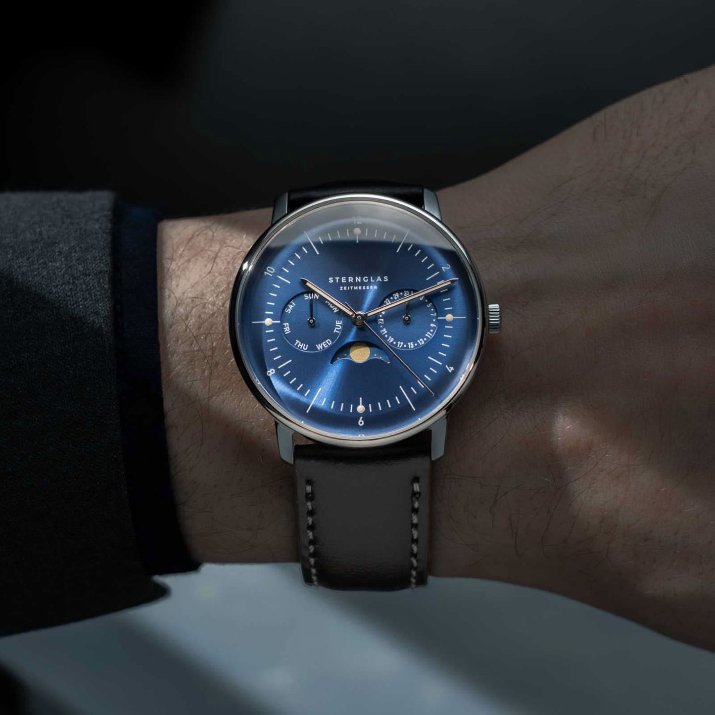 Montre pour homme au poignet : cadran bleu, bracelet en cuir noir, boîtier argenté.
