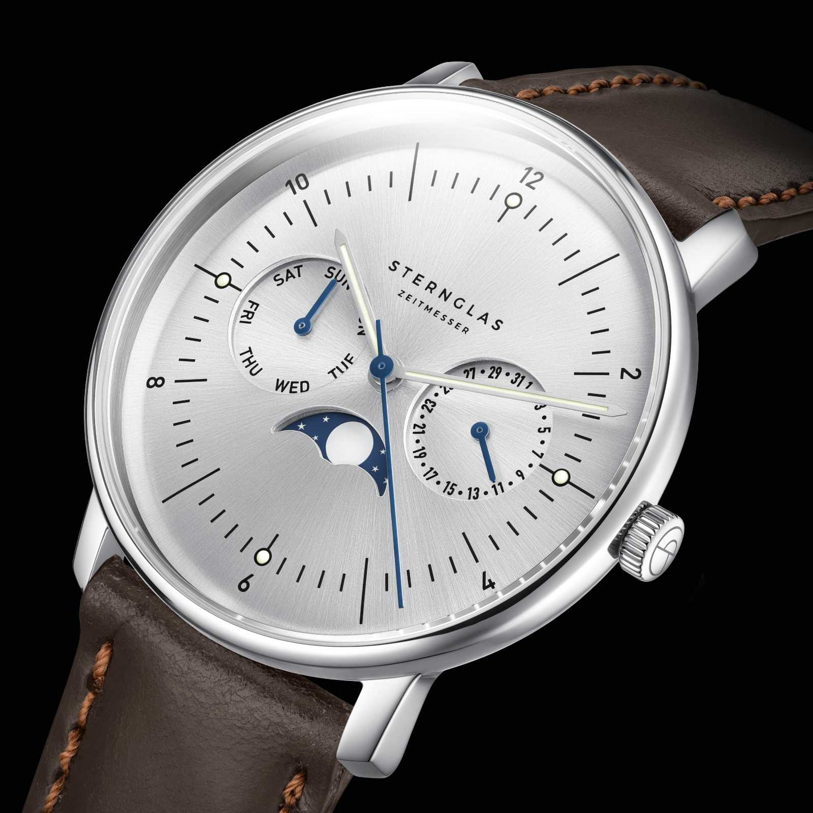Vue rapprochée d'une montre Sternglas pour homme : cadran argenté avec phase lunaire bleue, bracelet en cuir marron.