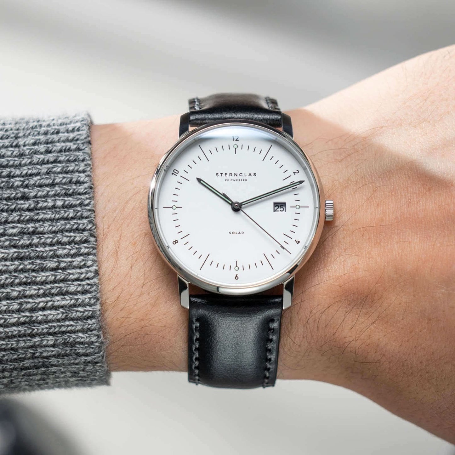 Montre-bracelet au poignet : bracelet en cuir noir, boîtier argenté, cadran blanc